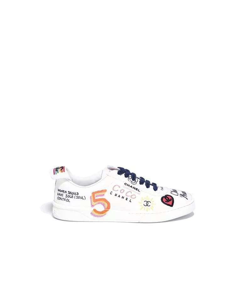 Chanel x Pharrell graffiti white canvas sneakers with blue and red shoe laces left foot in a full white background