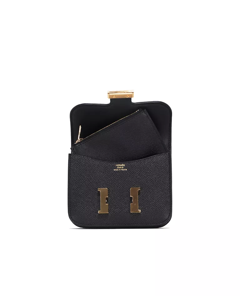 Portefeuille Hermès Constance Slim noir ouvert avec un petit sac à fermeture éclair à l'intérieur avec une quincaillerie dorée sur le devant sur fond blanc